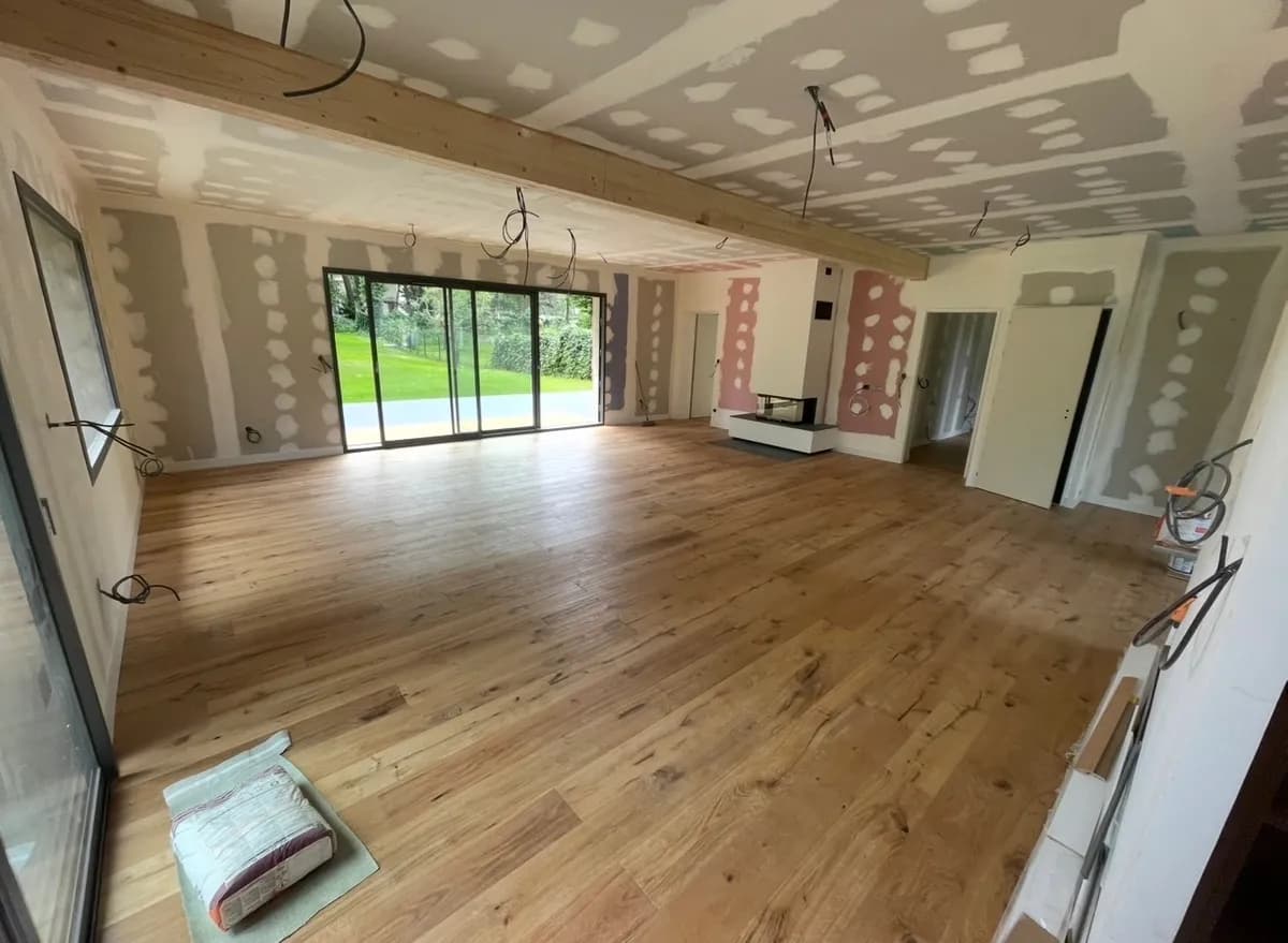 Grande pièce de vie rénovée : cloisons plâtrées, parquet bois et baie vitrée